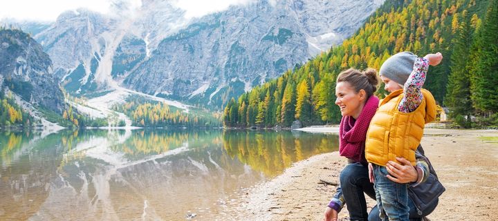 Mutter und Kind am herbstlichen Bergsee mit Blick auf verschneite Gipfel