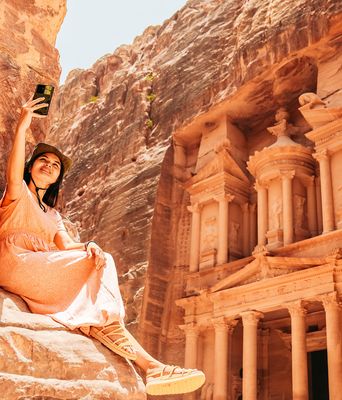Frau sitzt vor dem Schatzhaus in Petra und fotografiert sich