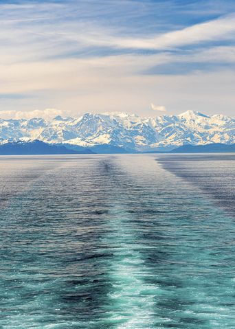Blick auf die Fahrspur eines Kreuzfahrtschiffs im Prince William Sound mit schneebedeckter Bergkulisse in Alaska