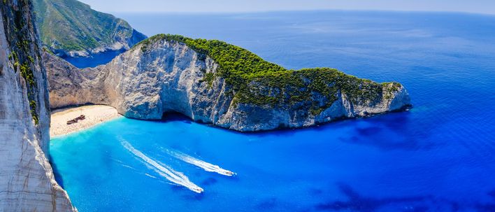 Blick auf den mit Felsen umrandeten Navagio Beach an himmelblauem Wasser mit Booten auf Zakynthos in Griechenland 