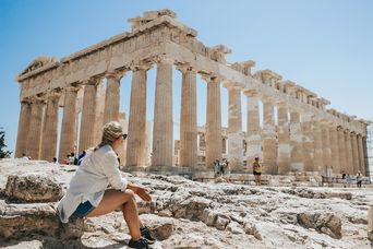 Frau sitzt vor Akropolis in Athen