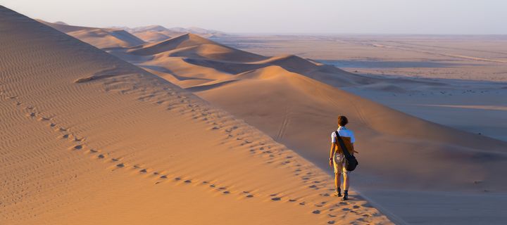 Person wandert durch hohe Dünen im Sossusvlei mit langen Schatten im Abendlicht