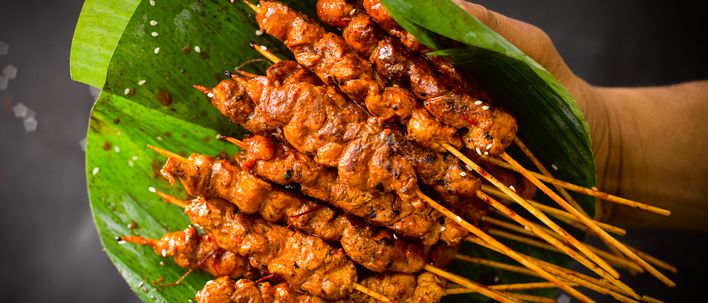 Gegrillte Saté-Spieße mit würziger Sauce liegen auf einem grünen Bananenblatt als indonesische Spezialität