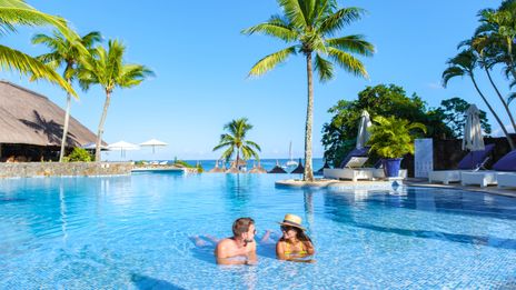 Paar entspannt im Pool eines Hotels auf Mauritius mit Palmen und Meerblick