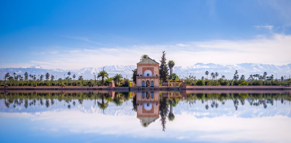 Haus im Menara Garten in Marrakesch in Marokko spiegelt sich im See bei blauem Himmel