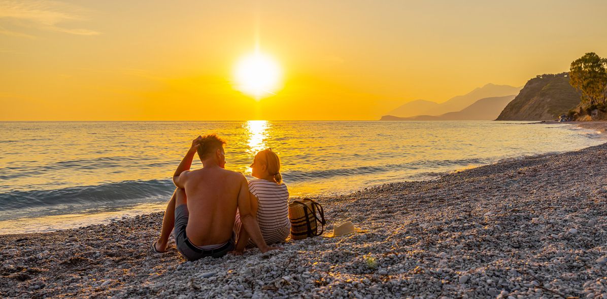 Paar sitzt am Strand und genießt den Sonnenuntergang an der Albanischen Riviera
