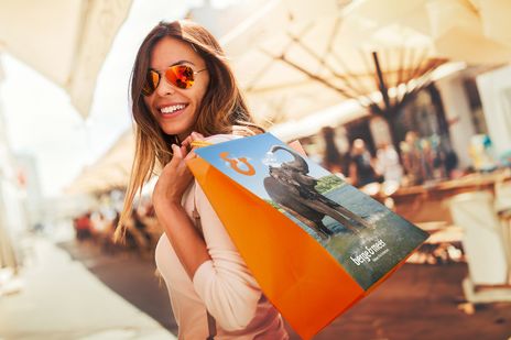 Frau mit Sonnenbrille trägt Einkaufstüte von Berge & Meer beim Bummeln im Einkaufszentrum