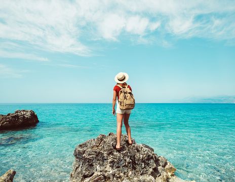 Frau steht auf Felsen am Meer und blickt in die Ferne bei klarem Himmel