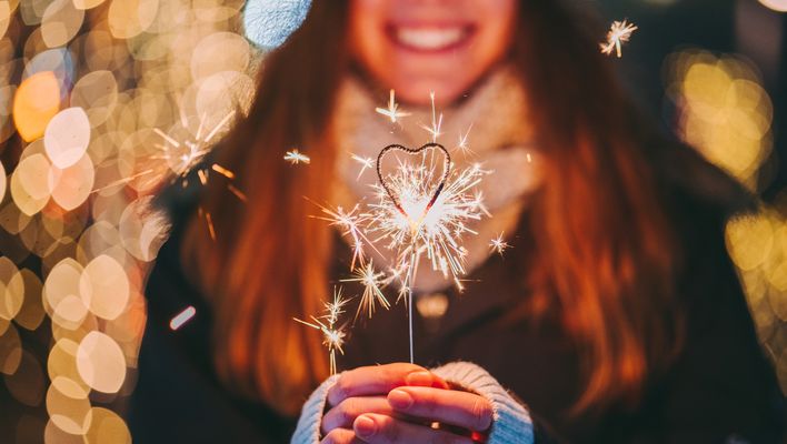 Junge Frau hält Wunderkerze in der Hand und lächelt in festlicher Stimmung