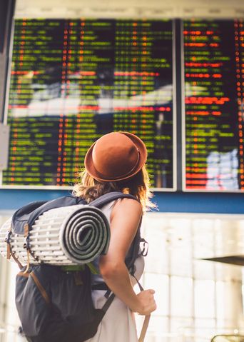 Frau mit Rucksack und Hut schaut auf die Abflugtafel im Flughafen