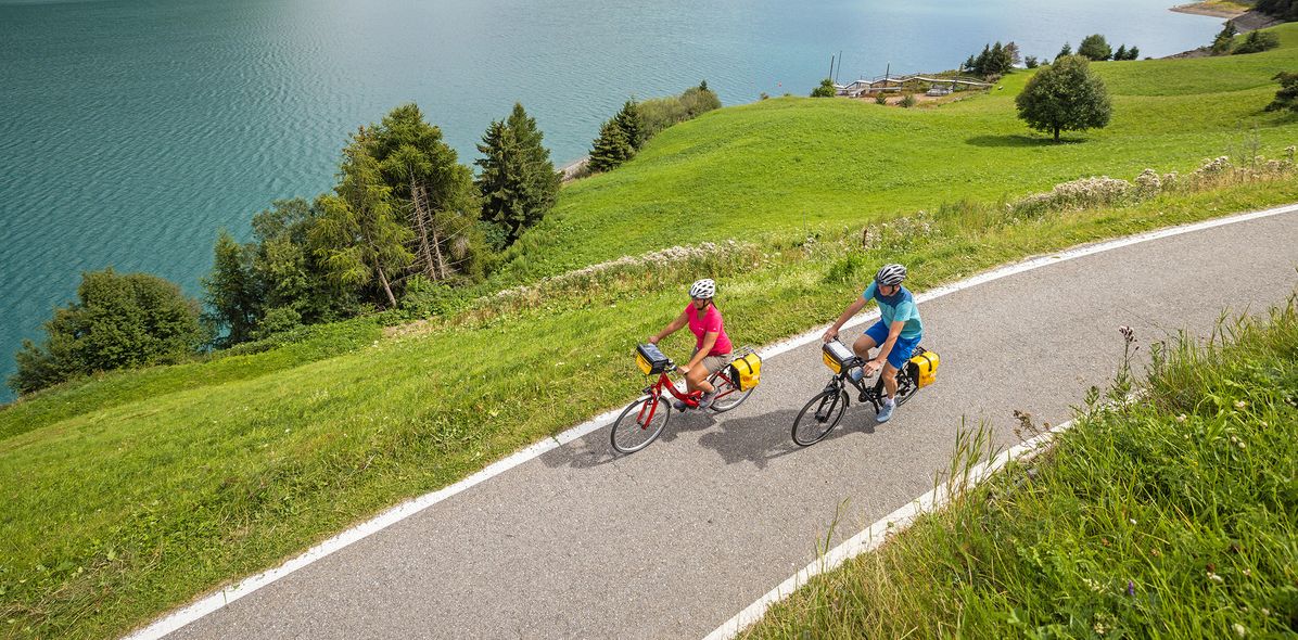 Zwei Radfahrer radeln an einem See auf einem Radweg im Sommer.