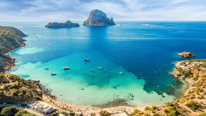 Blick auf die Bucht Cala d’Hort auf Ibiza mit der Felseninsel Es Vedrà im Hintergrund und türkisblauem Meer