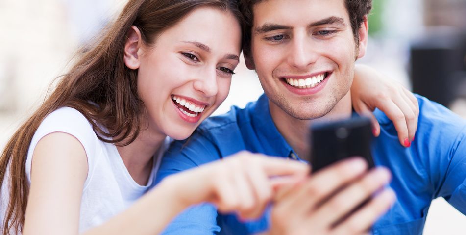 Frau und Mann gucken Arm in Arm interessiert in ein Handy und lachen