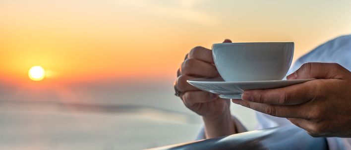 Frau genießt eine Tasse Kaffee auf dem Balkon eines Kreuzfahrtschiffs mit Blick auf das Meer bei Sonnenaufgang