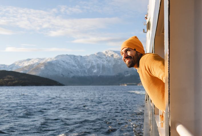 Ein lächelnder Mann lehnt sich aus einem Schiff und bewundert die wunderschöne verschneite Berglandschaft
