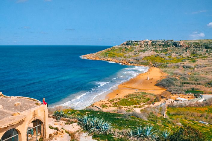 Eine Frau sitz auf dem Hausdach und blickt auf den goldenen Strand der Ramla Bay auf Gozo, Malta