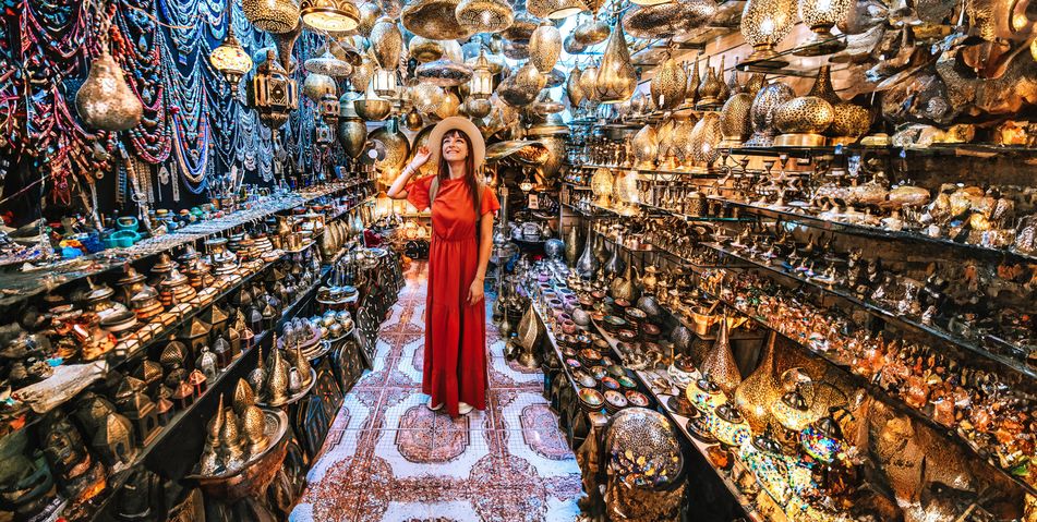 Frau im roten Kleid sieht sich in einem Souvenir-Shop in Marrakesch in Marokko um und hält mit einer Hand ihren Hut fest