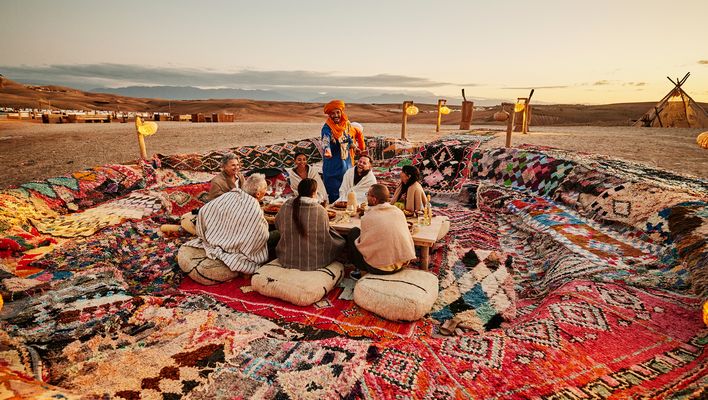 Großes Marktareal mit bunten Teppichen, Waren und vielen Menschen in Marrakesch