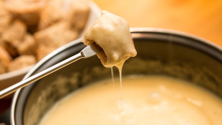 Cremiges Schweizer Käsefondue wird mit Brotstücken und einer langen Fonduegabel gemeinsam genossen.