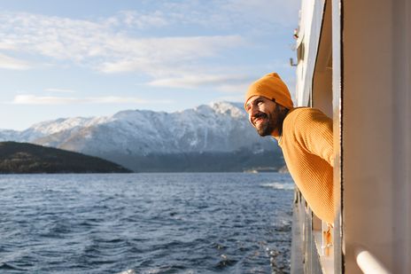 Ein lächelnder Mann lehnt sich aus einem Schiff und bewundert die wunderschöne verschneite Berglandschaft