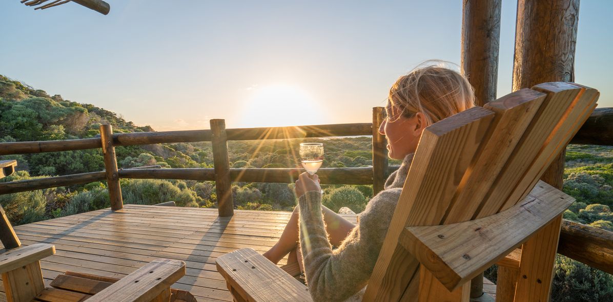 Frau sieht auf einer Terrasse und genießt den Sonnenuntergang mit einem Glas Wein