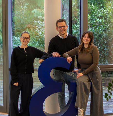 Drei Kollegen von Berge & Meer posieren vor dem Berge & Meer Superzeichen in der Lobby