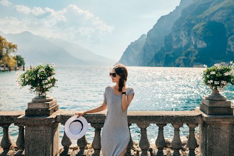 Frau in Sommerkleid und Hut steht an einer Promenade mit Blick auf den Gardasee