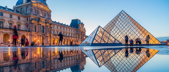 Louvre in Paris mit Glaspyramide und historischer Museumsfassade bei Sonnenuntergang