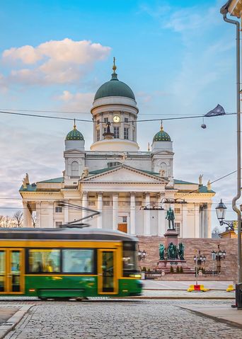Blick durch eine Gasse auf die Kathedrale von Helsinki mit einer vorbeifahrenden Straßenbahn im Vordergrund, Finnland