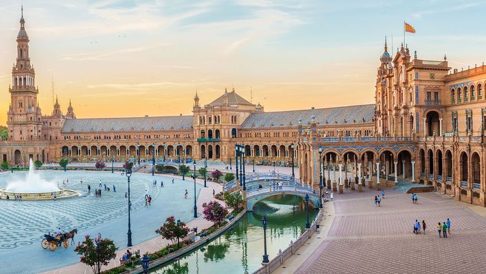 Weitläufige Ansicht der Plaza de España in Sevilla mit Halbkreisbau, Kanal und Brücken im Abendlicht