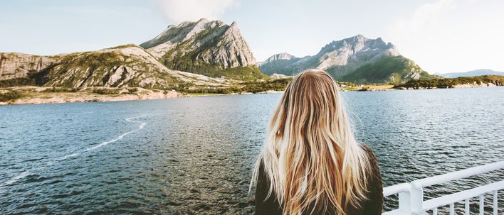 Eine Frau die an Bord eines Schiffes ist und auf Berge in Norwegen schaut