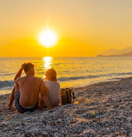Paar sitzt am Strand und genießt den Sonnenuntergang an der Albanischen Riviera