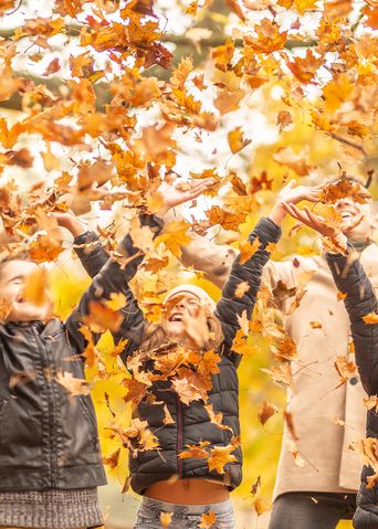 Familie wirft Herbstlaub in die Luft und lässt sich davon beregnen