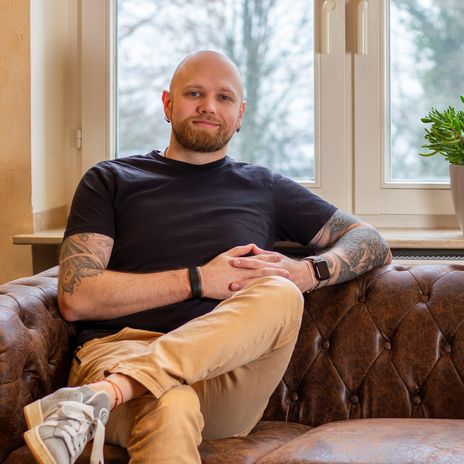 Abteilungsleiter Dennis sitzt gemütlich auf einer Couch und lächelt in die Kamera