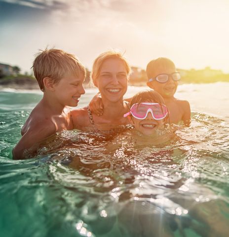 Mutter mit 3 Kindern spielen im Meer, tragen Schwimmbrillen und tauchen lachend auf