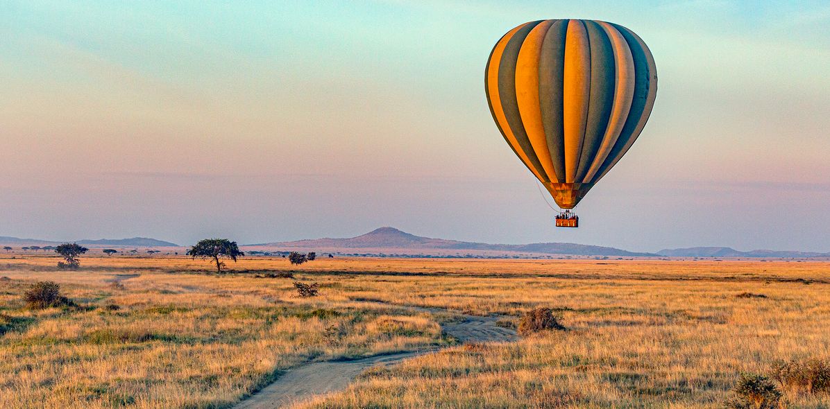 Heißluftballon fliegt bei Sonnenaufgang über den Serengeti Nationalpark in Tansania