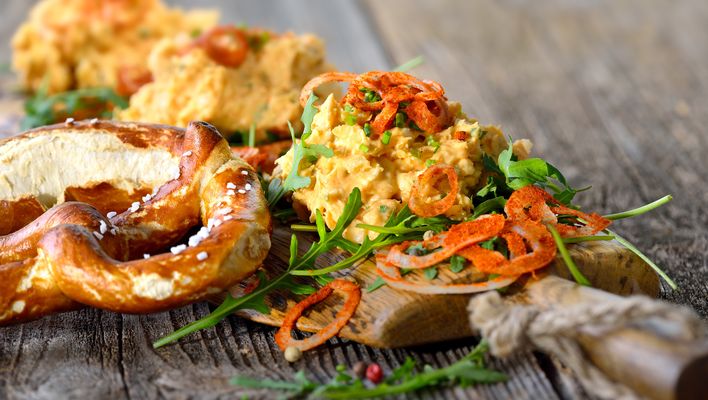 Bayerische Brezel mit Obatztem, Salat und geraspeltem Gemüse wird auf einem Holzteller serviert