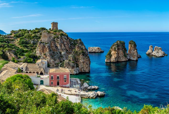 Blick auf eine idyllische Bucht mit Häusern und Felsen im Ort Scopello auf Sizilien