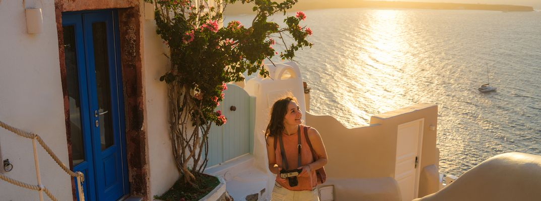 Frau mit einer Kamera in der Hand spaziert durch die Gassen von Santorin bei Sonnenuntergang