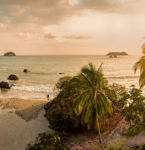 Tropischer Strand in Costa Rica bei Sonnenuntergang mit Palmen und Felsen am Wasser