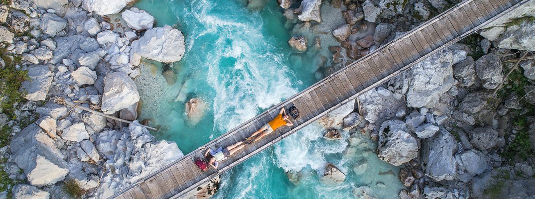 Türkisfarbener Fluss im Triglav-Nationalpark mit Hängebrücke und Felsbett