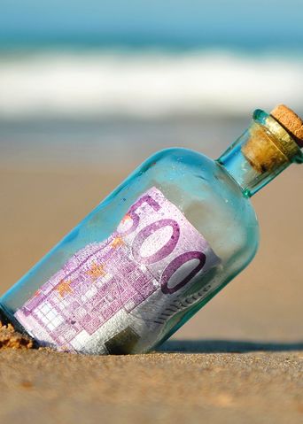 Flasche mit Korken und 500 € steckt im Strand, im Hintergrund Meer