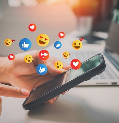 Mann hält Smartphone in der Hand mit Emojis über dem Display 