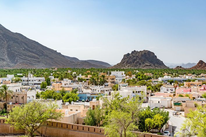 Blick über die Stadt Rustaq im Oman mit Palmen, Bergen und traditioneller Bebauung