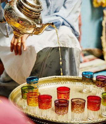 Marokkanischer Minztee wird aus einer silbernen Kanne in bunt verzierte Teegläser eingeschenkt