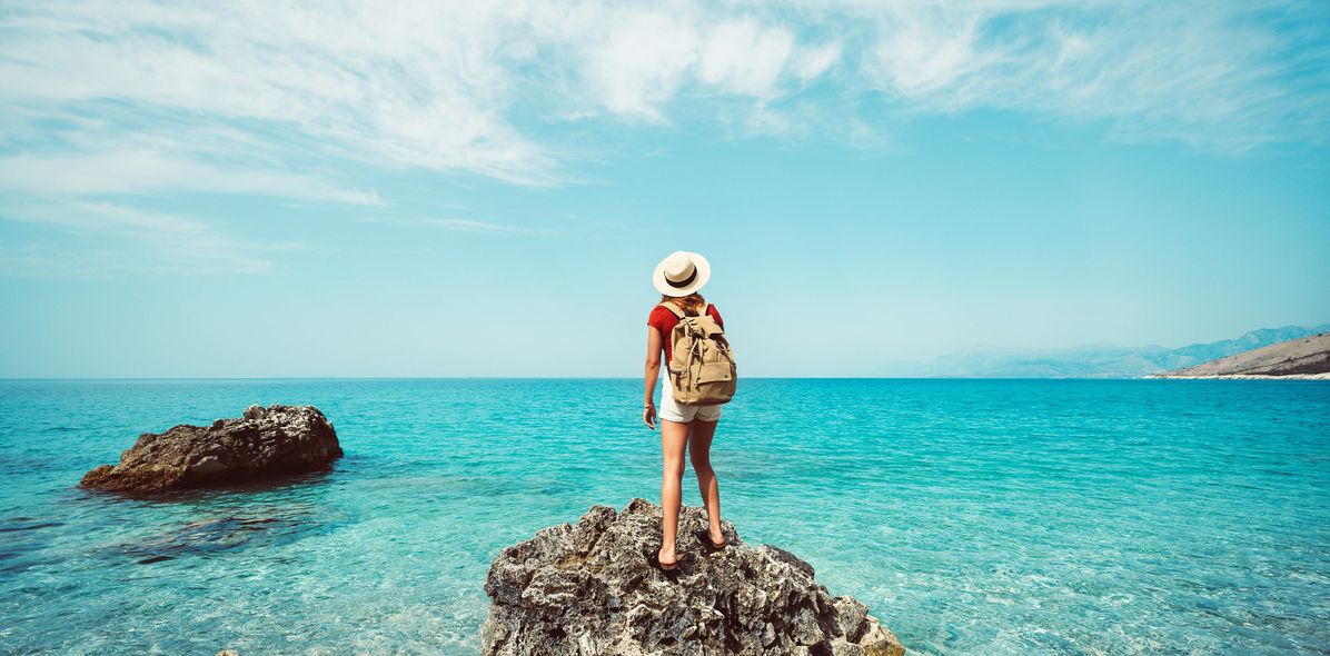 Frau auf einem kleinen Felsen im Meer blickt in die Ferne