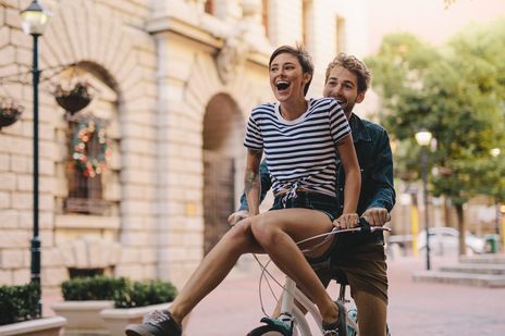 Paar fährt lachend mit dem Fahrrad durch die Stadt