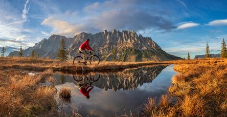 Ein Radfahrer fährt vorbei an einem See mit dem Hochkönig im Hintergrund, Österreich
