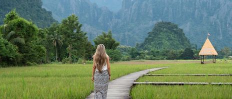 Frau spaziert an Reisfeldern entlang in Laos