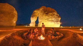 Wüstenlager bei Nacht mit Feuerstelle und beleuchteten Felsen in Saudi-Arabien